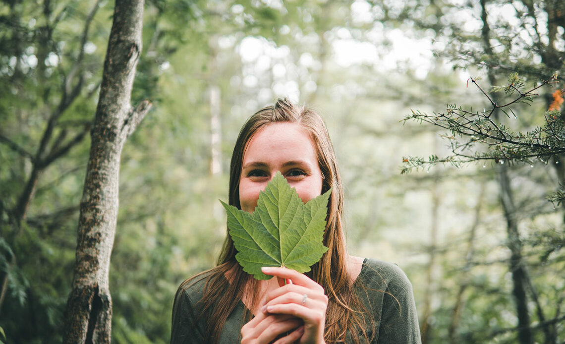 Eine junge Frau hält ein Baumblatt vor ihren Mund