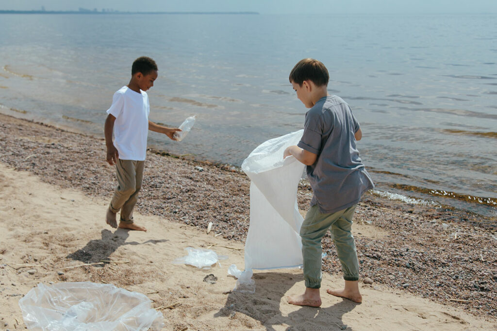 Zwei Jungen sammeln am Strand Plastikmüll in eine große Mülltüte