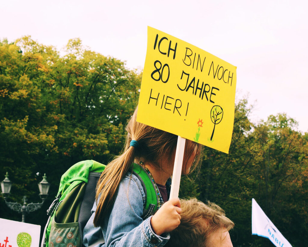Ein junges Mädchen hält bei einer Klimademonstration ein Schild mit der Aufschrift "Ich bin noch 80 Jahre hier" hoch