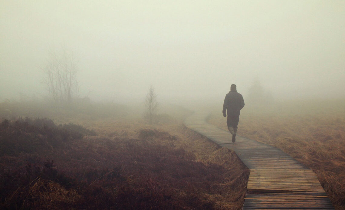Ein Mann wandert am frühen Morgen durch den Nebel über einem Moor