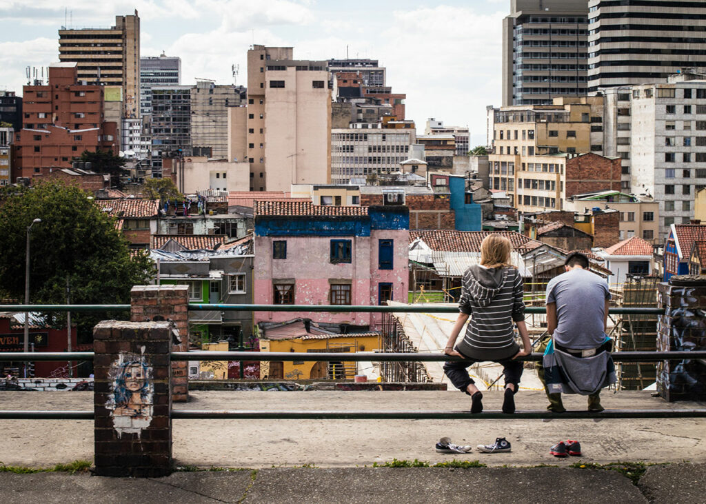 Zwei junge Menschen sitzen auf einem Geländer und schauen auf eine arme und runtergekommene Wohngegend