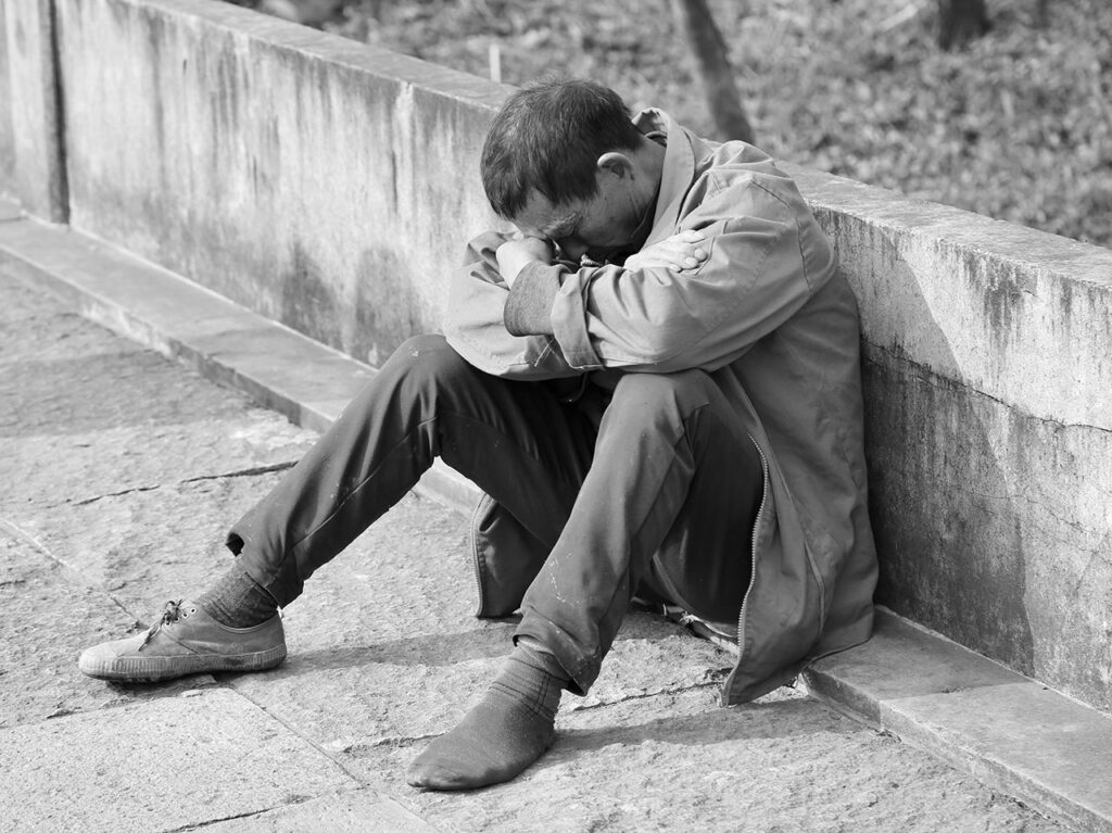Schwarz-Weiß -Aufnahme eines armen Mannes, der auf der Straße sitzt und dem der linke Schuh fehlt
