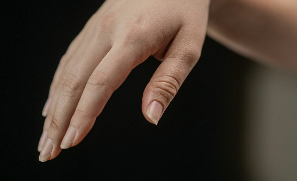 Die rechte Hand einer jungen Person vor schwarzen Hintergrund, die Fingernägel der Finger sind deutlich zu sehen