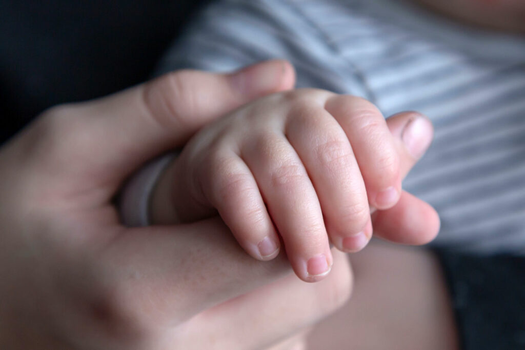 Die Hand eines Erwachsenen hält die Hand einen Babys, die kleinen Fingernägel deutlich sichtbar