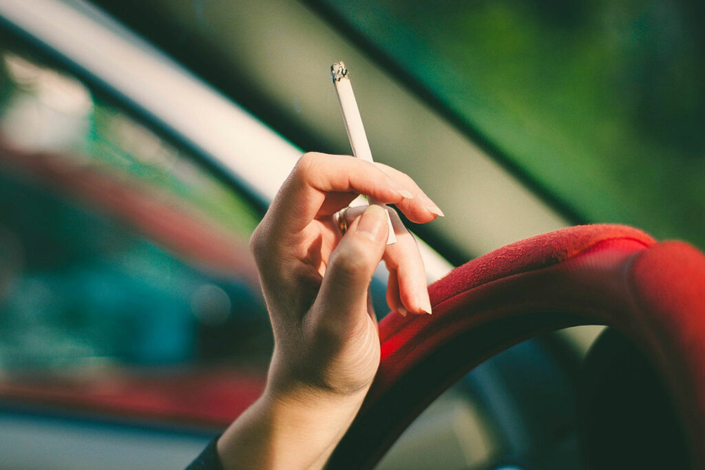 Eine Hand mit Zigarette und deutlich sichtbaren Fingernägeln am Steuer einen Autos