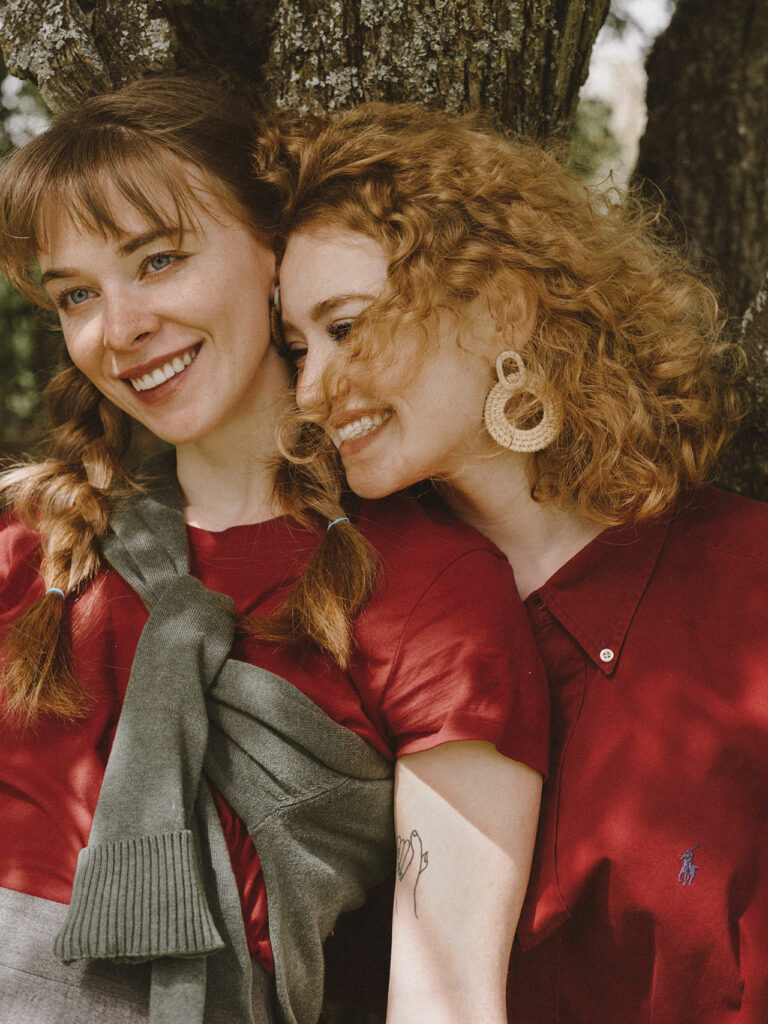 Zwei glückliche junge Frauen lachen an einem Baum lehnend