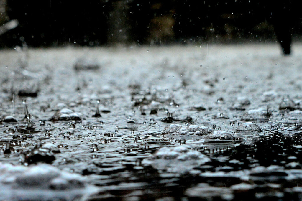 Regentropfen fallen auf den Boden und es bildet sich Regenwasser
