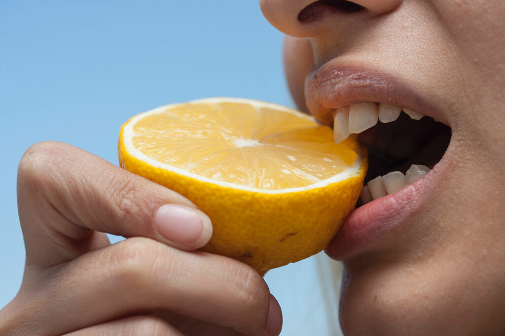 Eine Person mit gesunden Fingernägeln beißt in eine Zitrone, die viel Vitamin C enthält