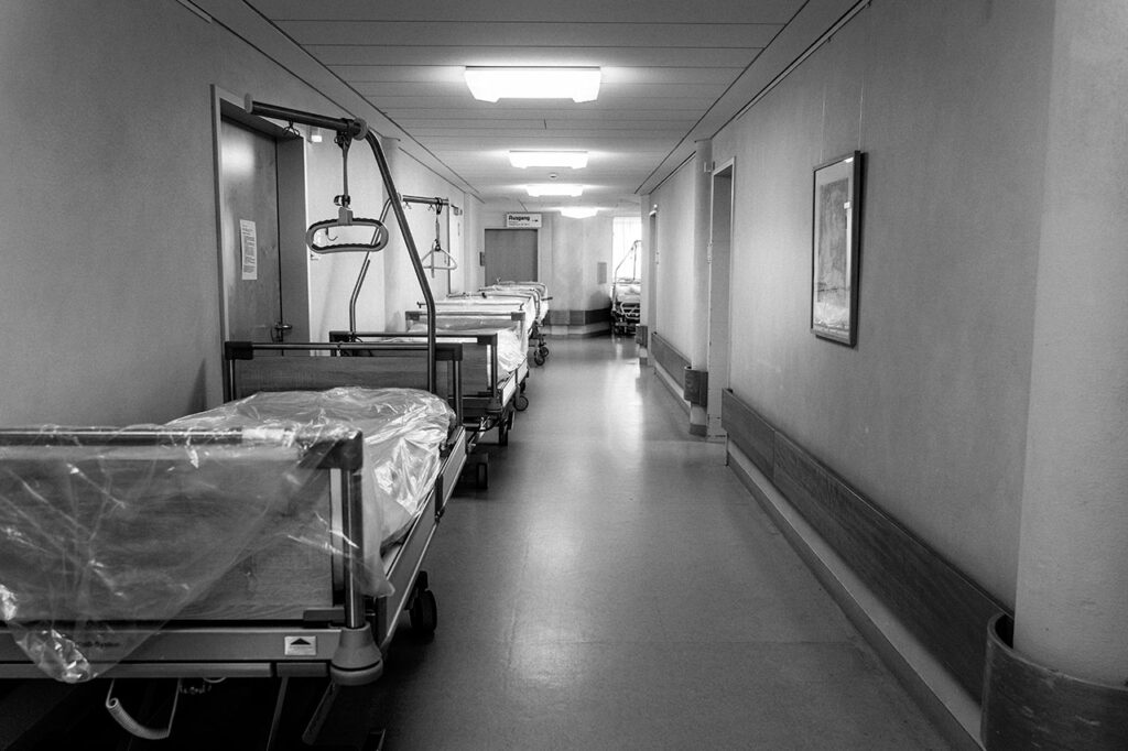 Blick in den Flur eines Krankenhauses, auf der linken Seite des Flurs stehen Krankenbetten