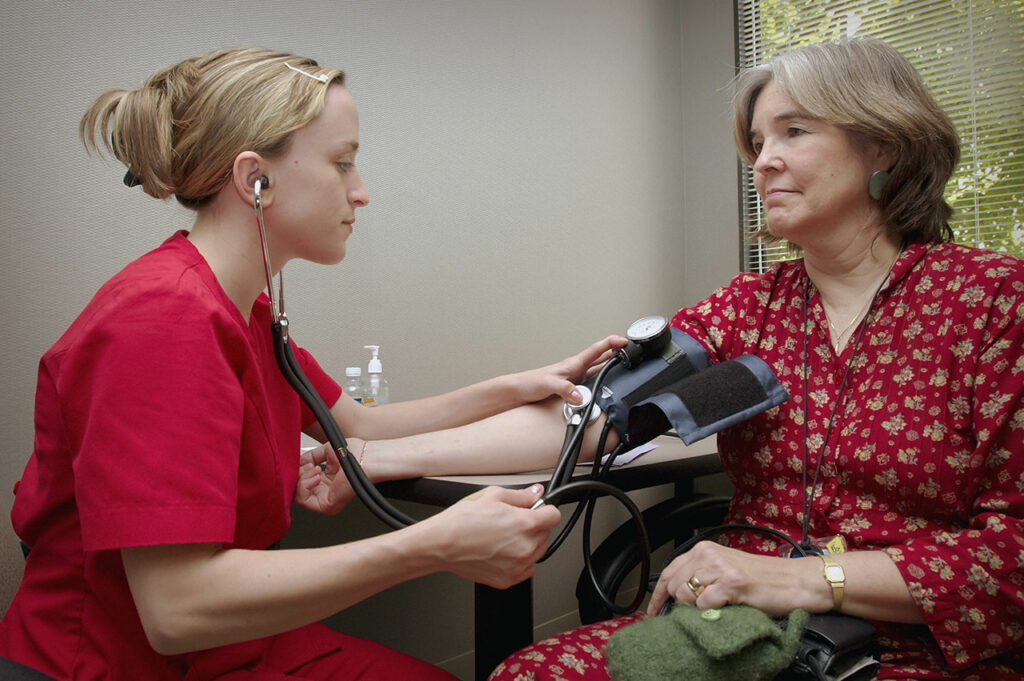 Einer älteren Dame wird durch eine junge Krankenschwester der Blutdruck gemessen