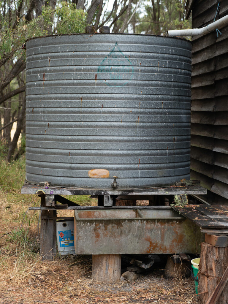 Ein Auffangbehälter aus Metall, der über eine Regenrinne das Regenwasser vom Dach einen Holzhauses auffängt