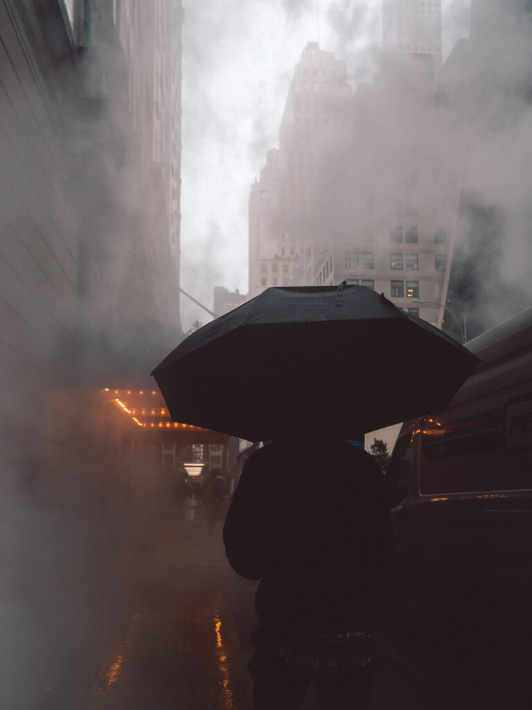 Eine Person mit Regenschirm geht durch den Smog und die Abgase einer Stadt
