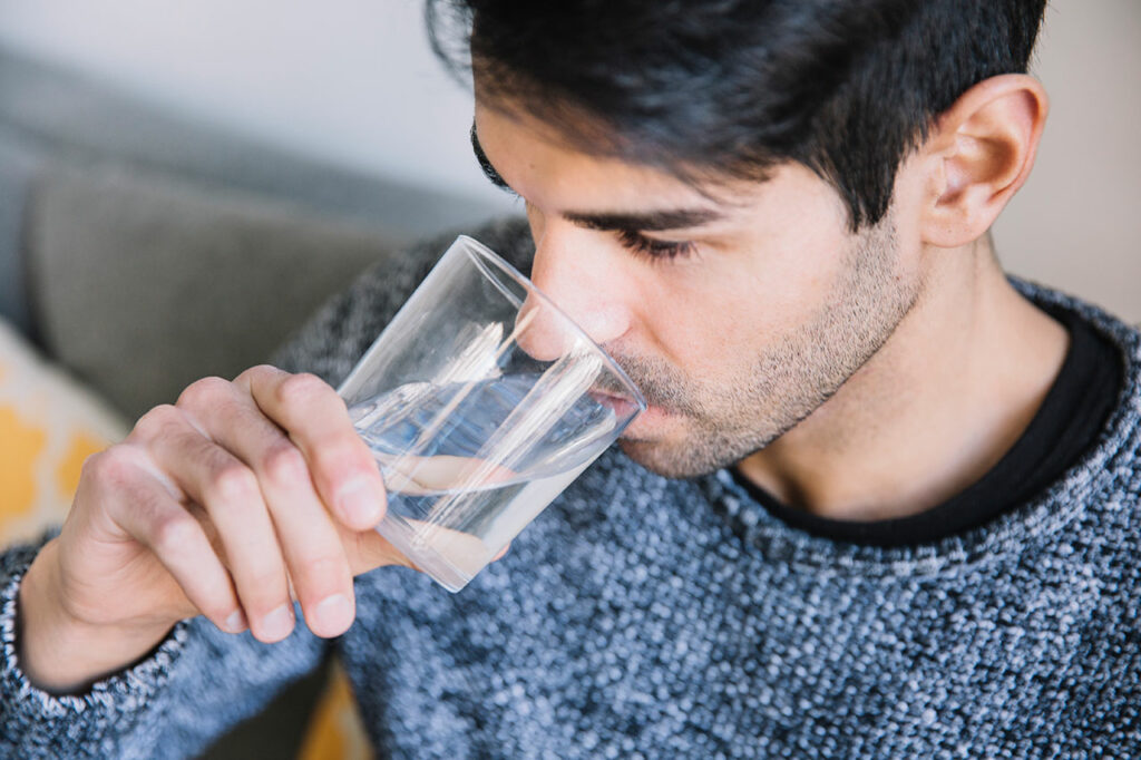 Ein junger Mann riecht an seinem Wasser aus dem Glas und prüft den Geschmack