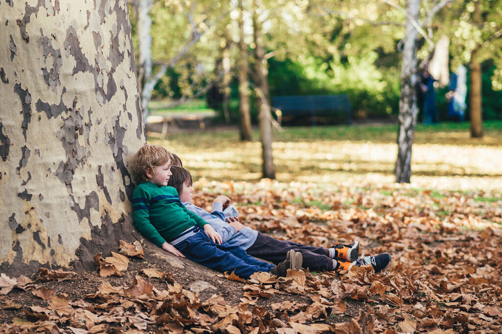 Mehrere Kinder lehnen sich glücklich und erschöpft an einem Baumstamm an
